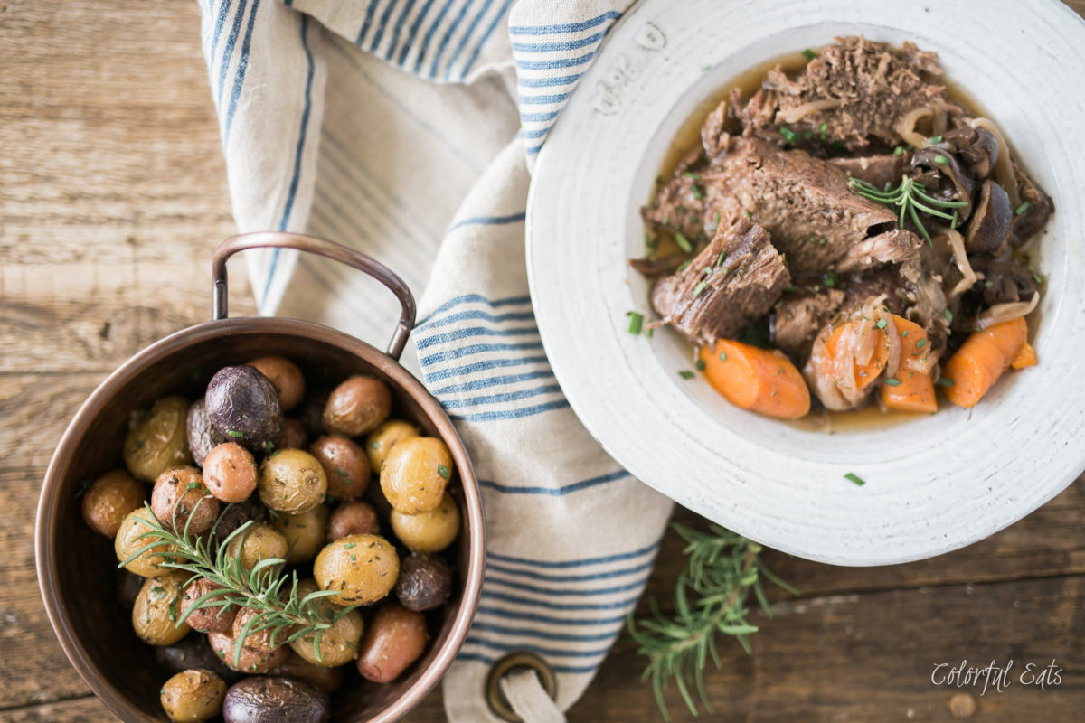 Image shows two plates with finished pot roast with duck fat rosemary potatoes served on them.
